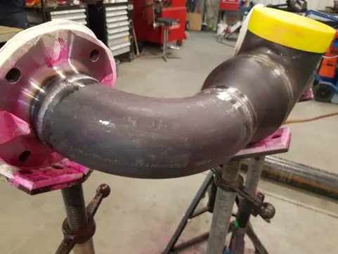 Gelaste leidingbocht met keuringsmarkeringen in de werkplaats in Linne