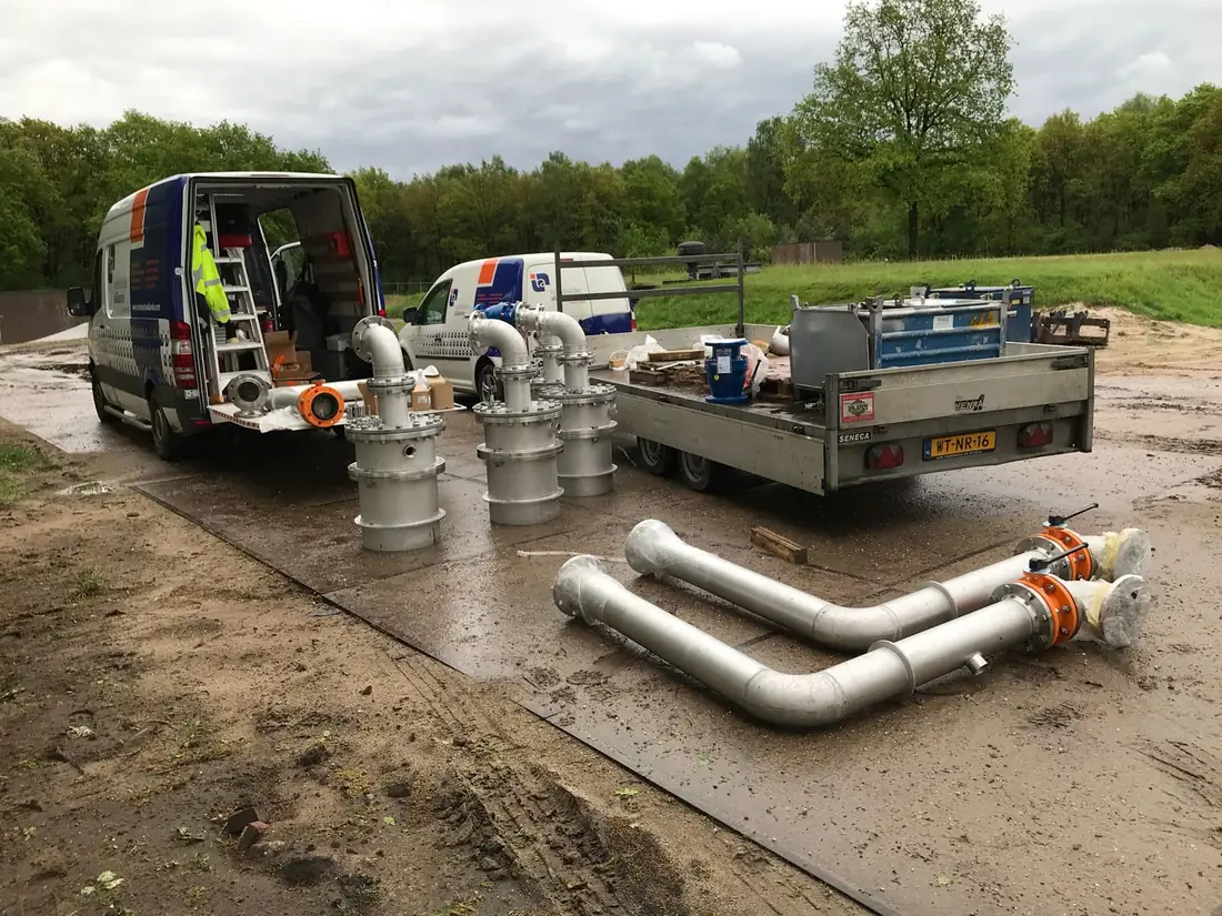 Gefabriceerde RVS-putkoppen en leidingdelen op een aanhanger naast een servicebus