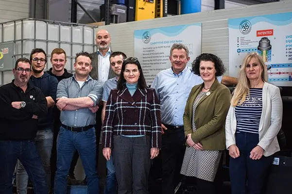 Groepsfoto van elf medewerkers van Technische Alliantie in de werkplaats, voor een waterbehandelingsinstallatie
