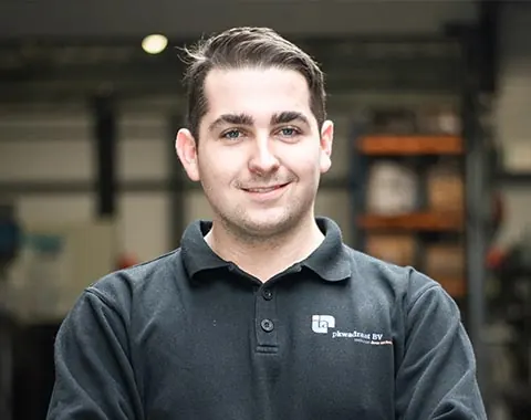 Portret van een jonge monteur in een donkere polo met het logo, in de werkplaats