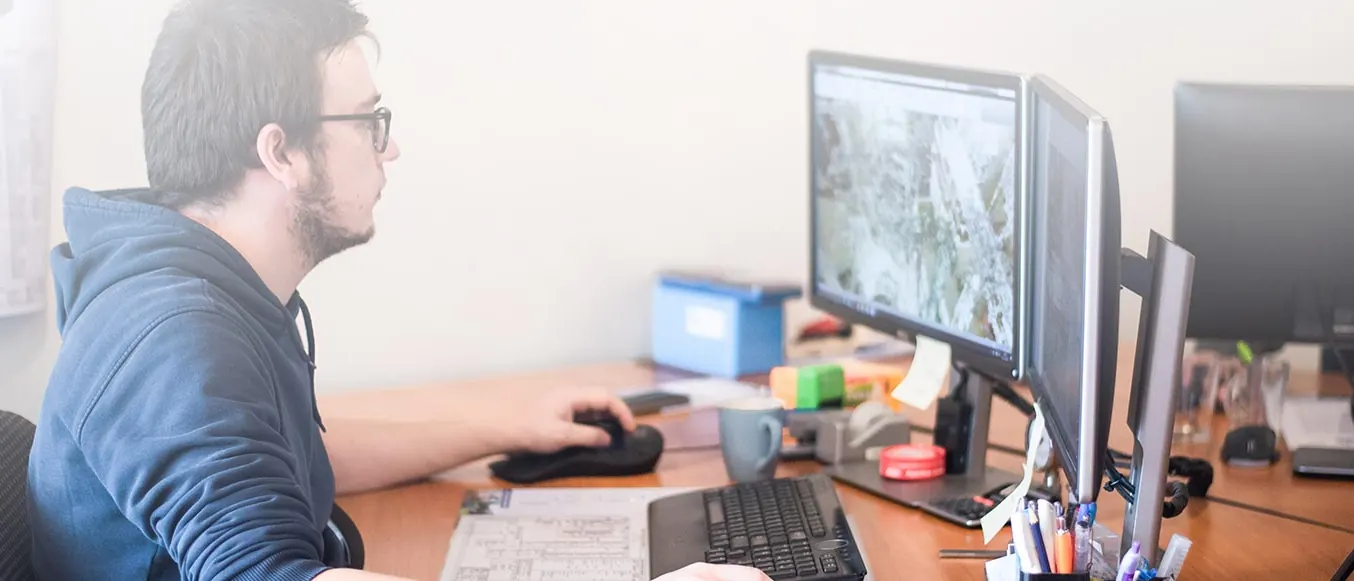 Engineer van Technische Alliantie aan een bureau met meerdere beeldschermen en tekeningen aan de wand