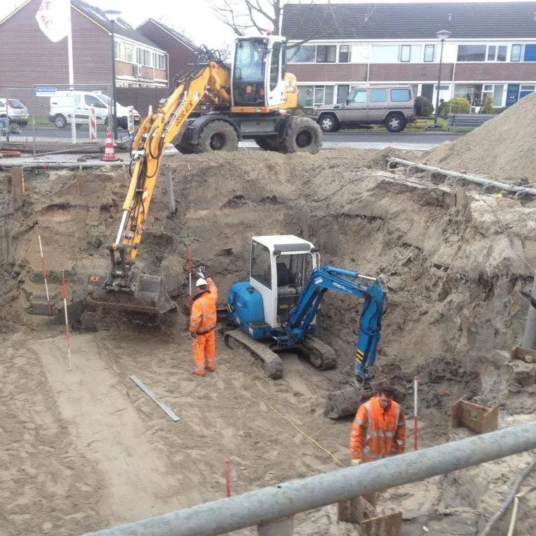 Graafmachines en werklieden bij een open sleuf voor een leiding in een woonstraat