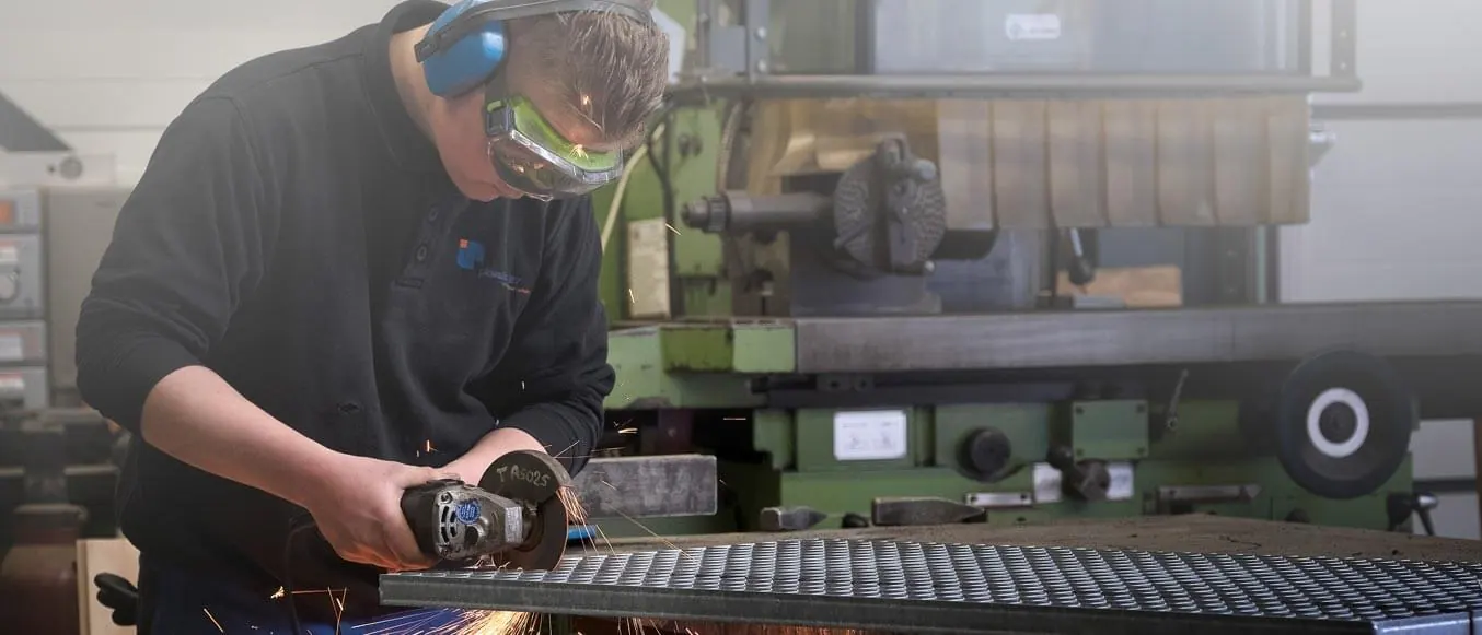 Medewerker met gehoorbescherming slijpt een metalen rooster in de werkplaats
